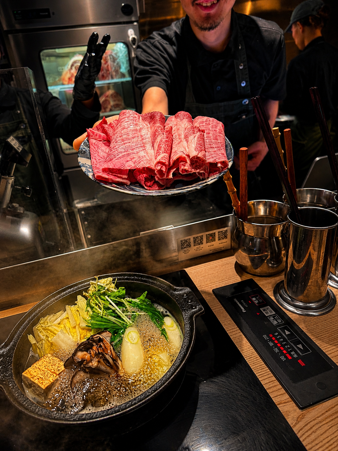 A chef presenting a plate of marbled wagyu over a steaming hot pot at Tominojo