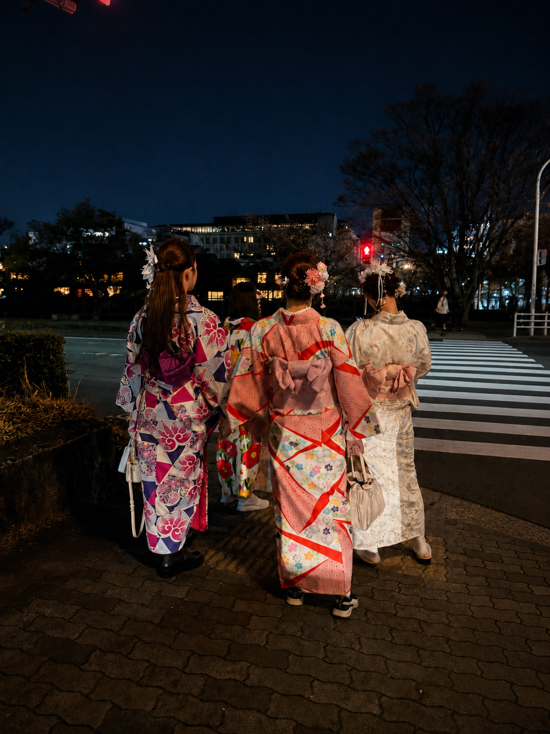 A group of women in colorful kimono seen from behind at a night crosswalk