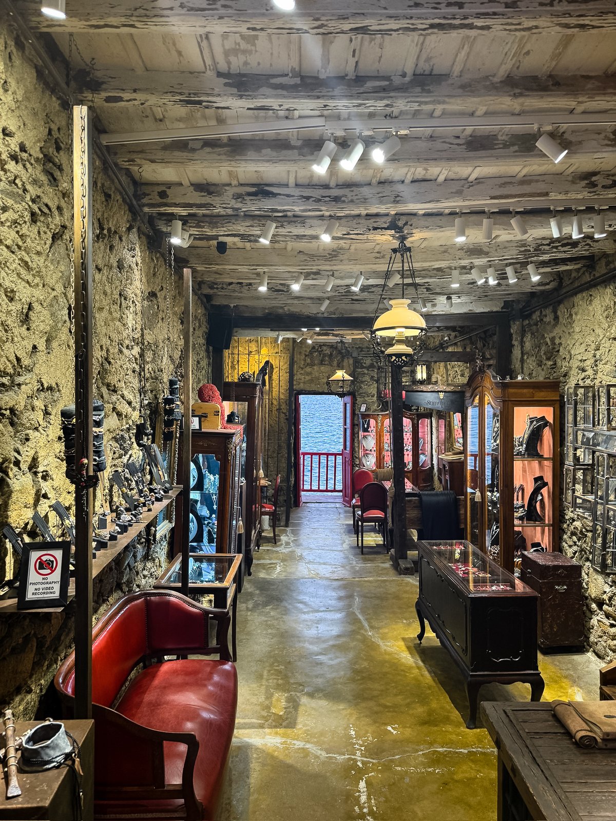 Interior of an atmospheric stone-walled jewelry shop in Little Venice, the sea framed in a red doorway at the far end