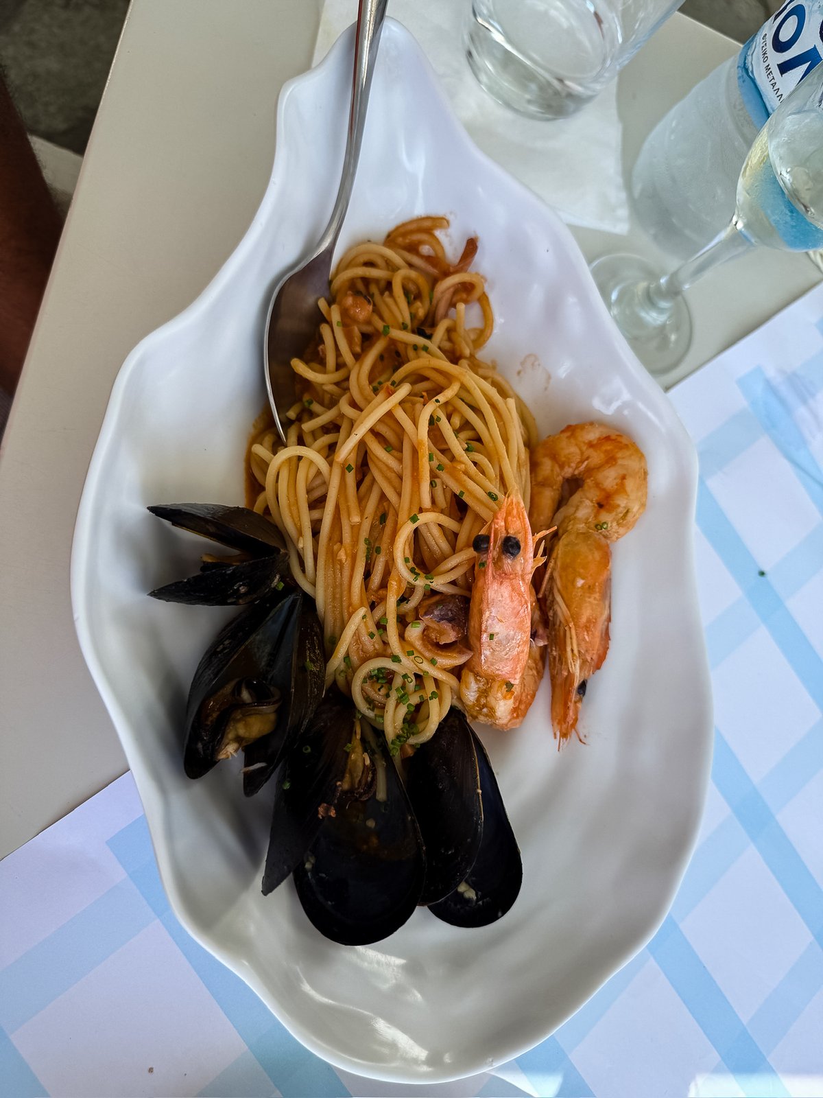 A white platter of seafood spaghetti in tomato sauce with whole prawns and black mussels