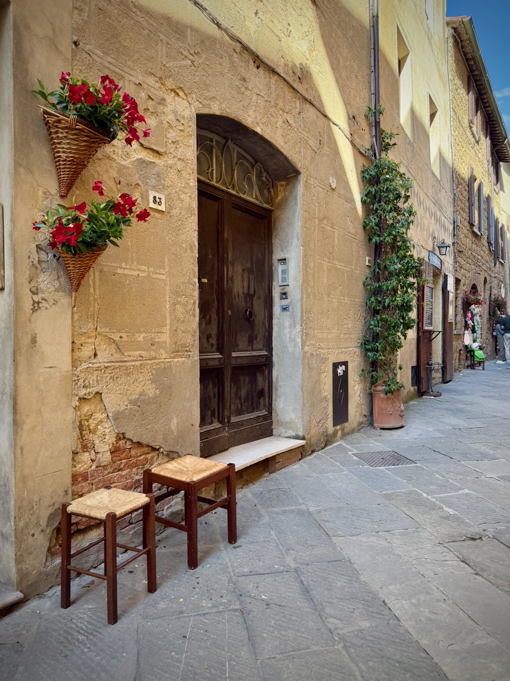 A doorway in Pienza with flower baskets and two straw stools